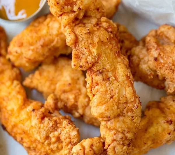 Crispy chicken tenders served with dipping sauce on a plate.